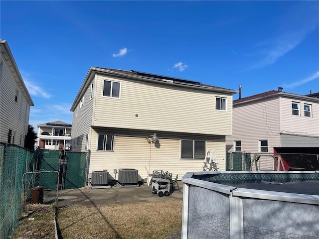 back of house with roof mounted solar panels, central AC, a fenced backyard, and a gate