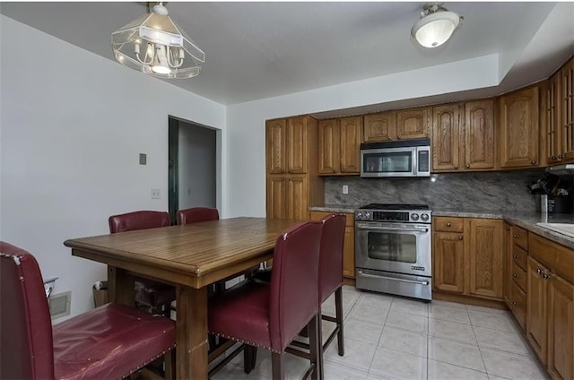 kitchen featuring light tile patterned floors, stainless steel appliances, brown cabinets, and backsplash