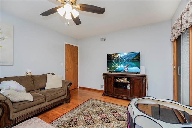 living area featuring a ceiling fan, visible vents, baseboards, and wood finished floors