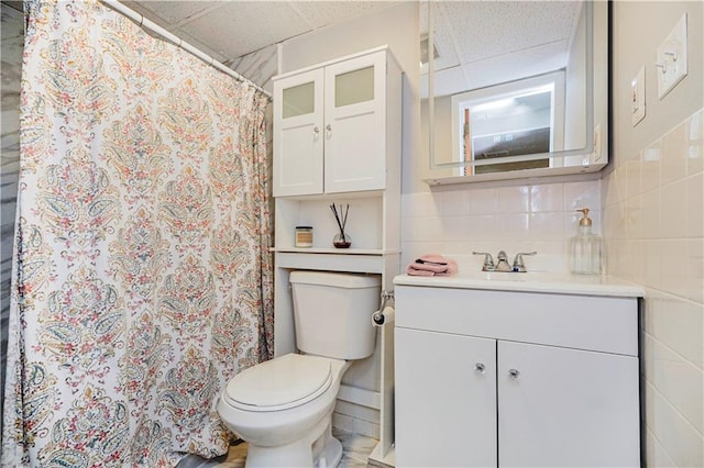 bathroom featuring tile walls, tasteful backsplash, a paneled ceiling, toilet, and vanity