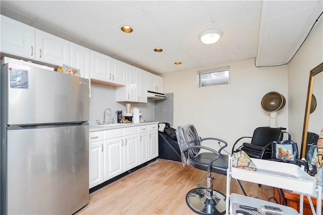 kitchen featuring light wood finished floors, light countertops, freestanding refrigerator, white cabinets, and a sink