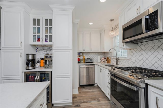 kitchen with wood finished floors, a sink, stainless steel appliances, white cabinetry, and decorative light fixtures