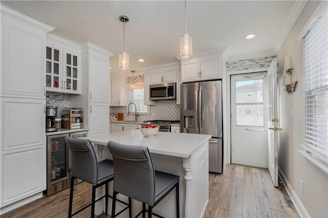 kitchen featuring beverage cooler, a sink, decorative backsplash, stainless steel appliances, and white cabinets