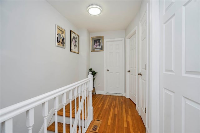 hallway featuring wood finished floors, an upstairs landing, and baseboards