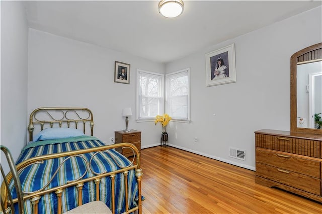 bedroom featuring arched walkways, wood finished floors, visible vents, and baseboards