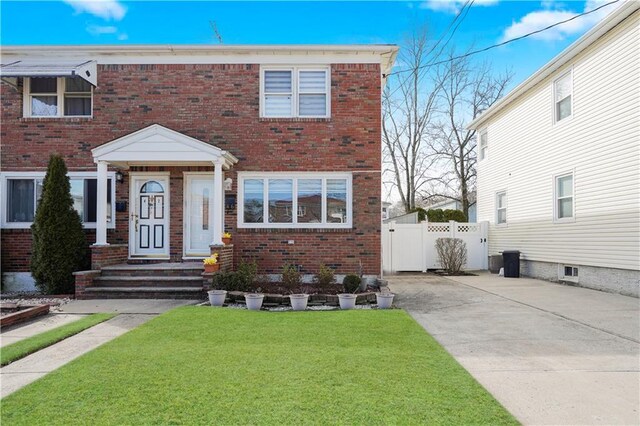 view of front of home with a front yard, a gate, fence, driveway, and brick siding