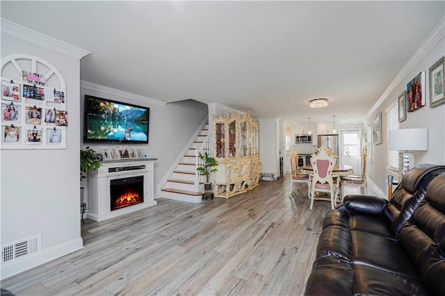 living area with light wood-type flooring, visible vents, a lit fireplace, crown molding, and stairs