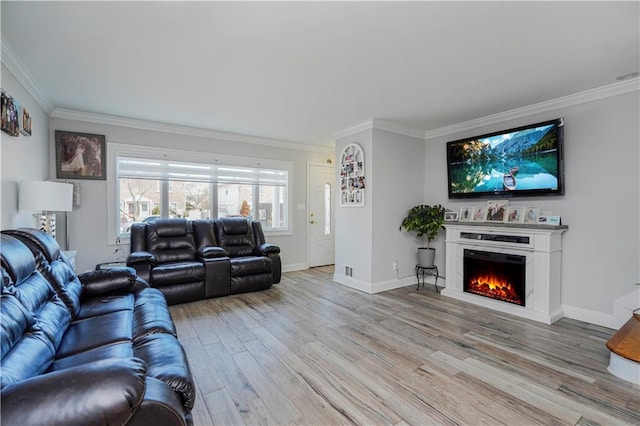 living area with wood finished floors, baseboards, a warm lit fireplace, and ornamental molding