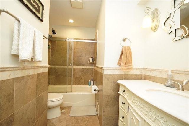 full bathroom with a wainscoted wall, tile walls, toilet, and combined bath / shower with glass door