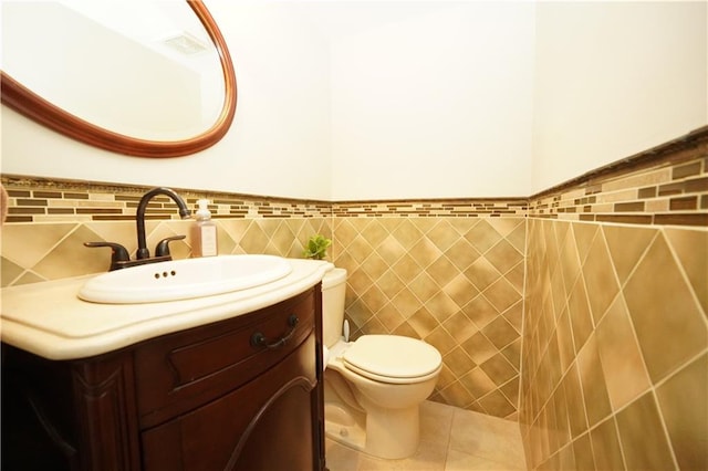 bathroom featuring vanity, a wainscoted wall, tile patterned floors, toilet, and tile walls