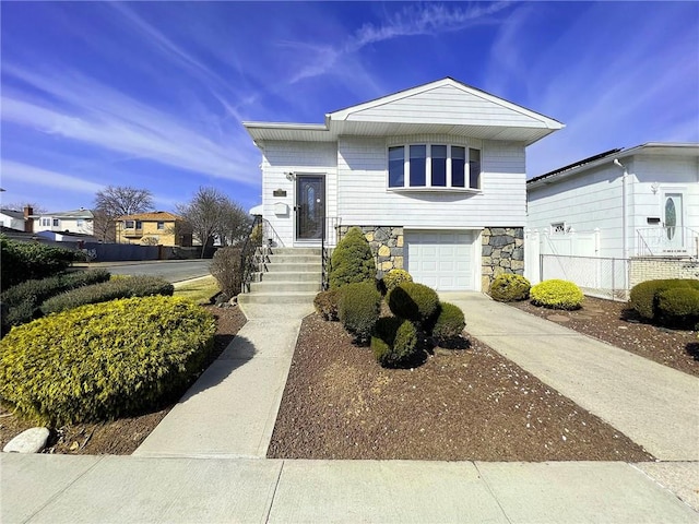 view of front of house featuring stone siding, an attached garage, fence, and driveway