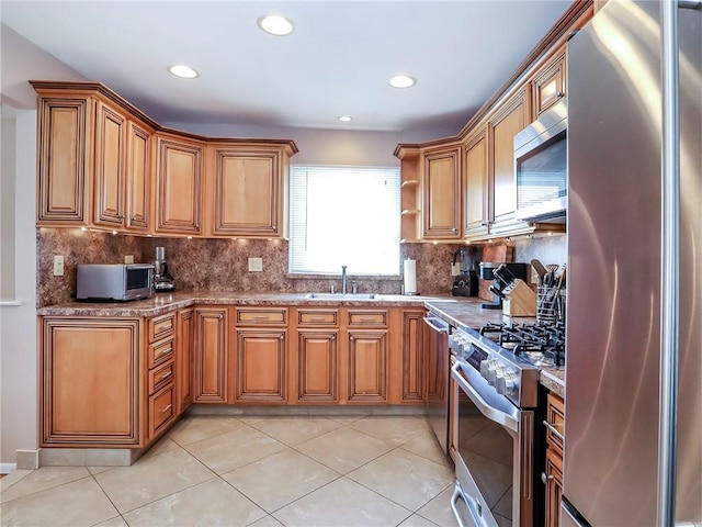 kitchen featuring stainless steel appliances, tasteful backsplash, brown cabinetry, a sink, and light stone countertops