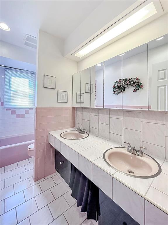 full bathroom with toilet, double vanity, tile walls, and a sink