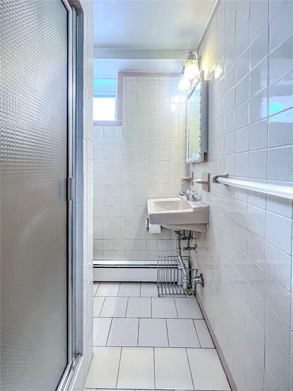 bathroom with tile walls, a baseboard radiator, a stall shower, a sink, and tile patterned flooring