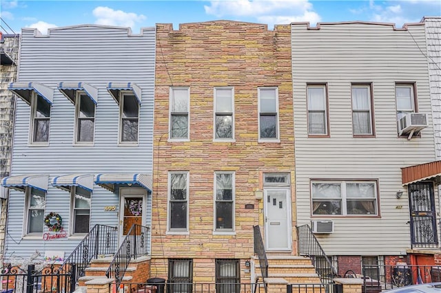 multi unit property featuring a fenced front yard, stone siding, an AC wall unit, and cooling unit