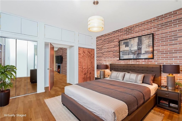 bedroom featuring light wood finished floors, brick wall, and a fireplace