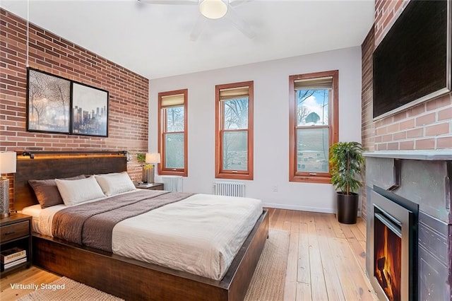 bedroom with a ceiling fan, radiator, light wood-style floors, brick wall, and baseboards