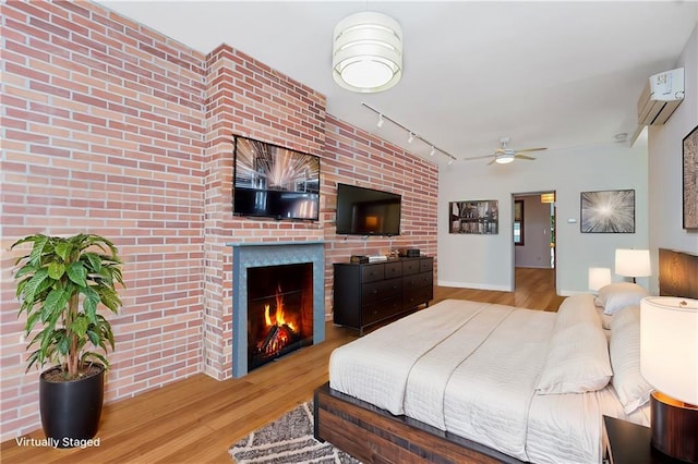 bedroom with a warm lit fireplace, an AC wall unit, wood finished floors, and track lighting