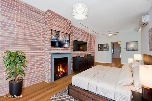 bedroom featuring a lit fireplace, track lighting, a wall unit AC, and wood finished floors