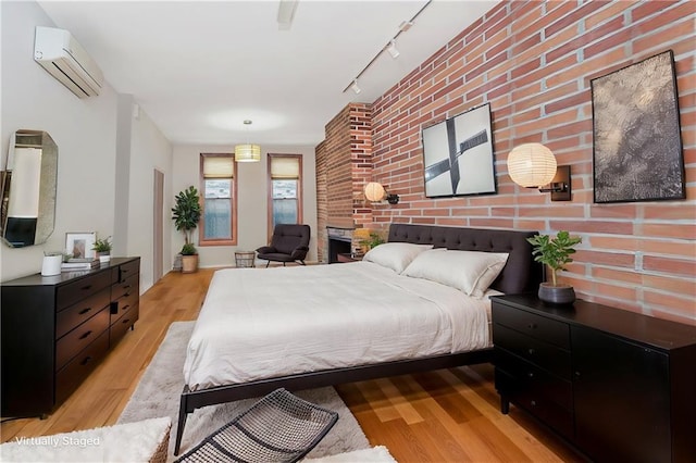 bedroom featuring brick wall, light wood-style flooring, track lighting, and a wall mounted AC