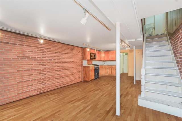 finished basement with track lighting, brick wall, stairway, and light wood-style floors