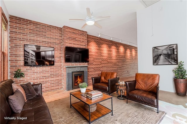 living room with ceiling fan, wood finished floors, a brick fireplace, and brick wall