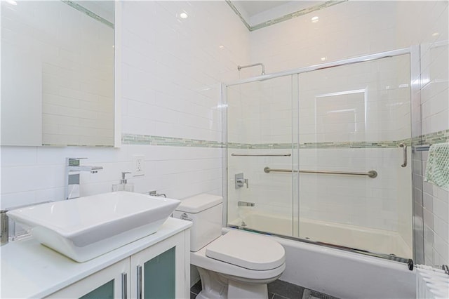 bathroom with backsplash, toilet, vanity, combined bath / shower with glass door, and tile walls