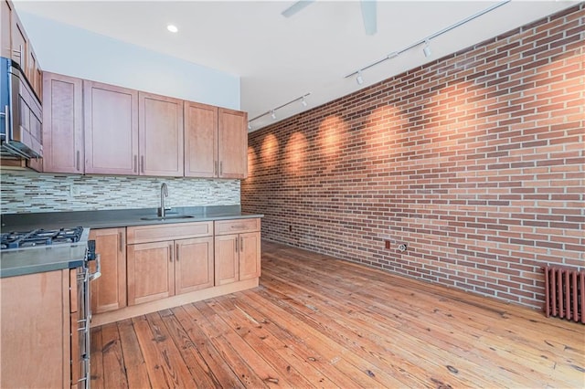 kitchen featuring a sink, backsplash, light wood-style floors, brick wall, and gas range