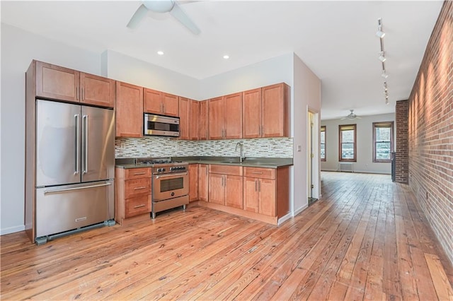 kitchen featuring ceiling fan, high quality appliances, light wood-style floors, backsplash, and dark countertops