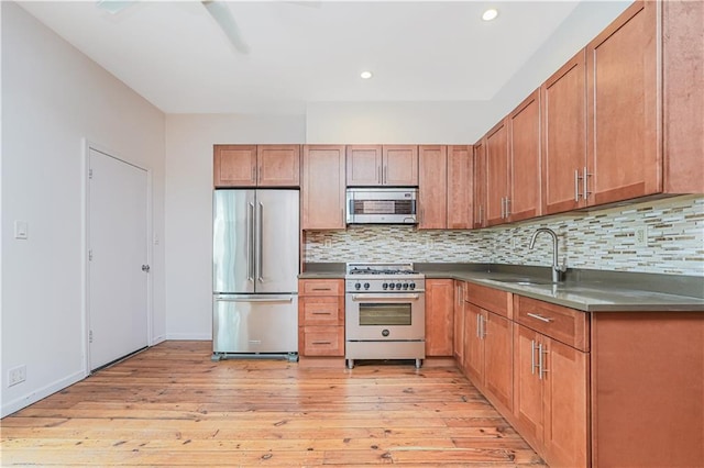 kitchen with high end appliances, light wood-type flooring, a sink, and tasteful backsplash