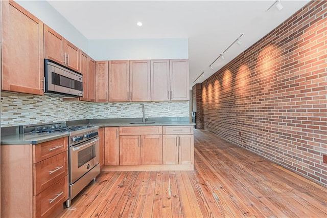 kitchen featuring decorative backsplash, brick wall, appliances with stainless steel finishes, light wood-type flooring, and a sink