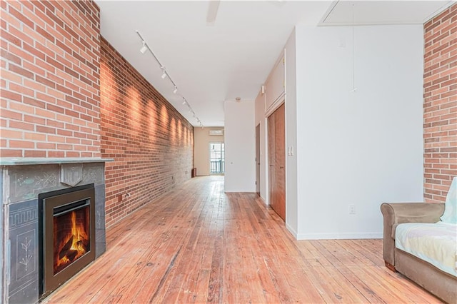 hall with track lighting, attic access, light wood-style flooring, and brick wall