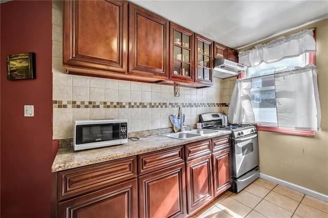 kitchen with white microwave, stainless steel range with gas cooktop, under cabinet range hood, a sink, and backsplash
