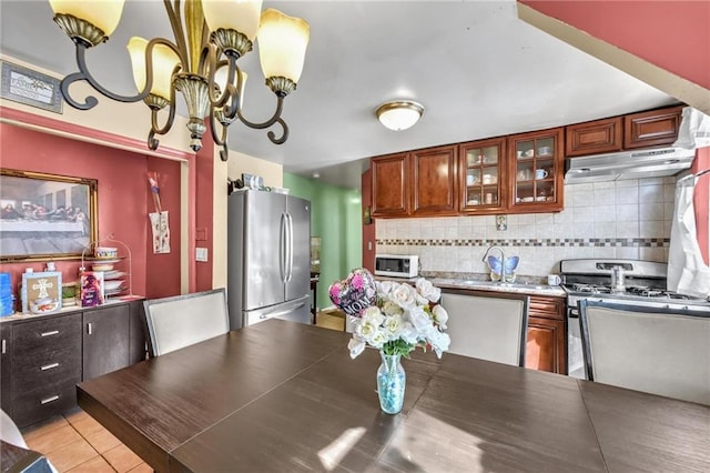 kitchen featuring under cabinet range hood, a sink, backsplash, light tile patterned floors, and stainless steel appliances