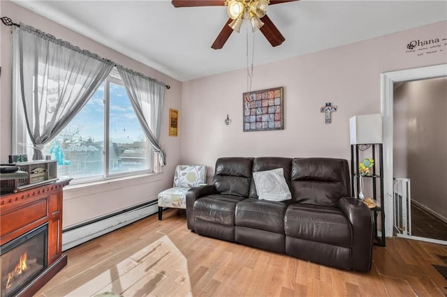 living room with a ceiling fan, a glass covered fireplace, wood finished floors, and a baseboard radiator