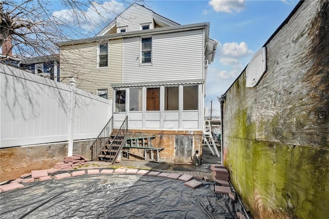 back of property with a sunroom, a patio area, fence, and stairway