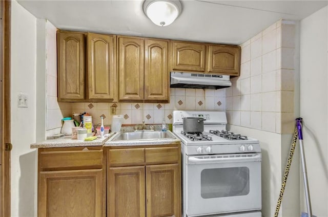 kitchen with gas range gas stove, light countertops, under cabinet range hood, a sink, and backsplash