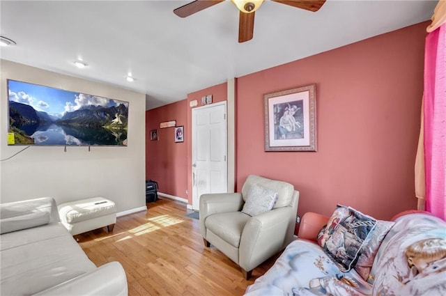 living area with baseboards, a ceiling fan, and light wood-style flooring