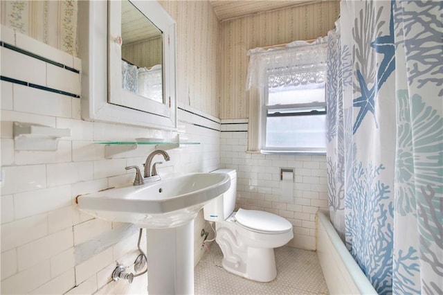 bathroom with toilet, tile walls, wainscoting, tile patterned floors, and wallpapered walls