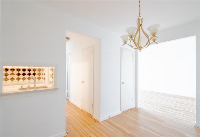 corridor featuring a sink, light wood-style flooring, and a notable chandelier