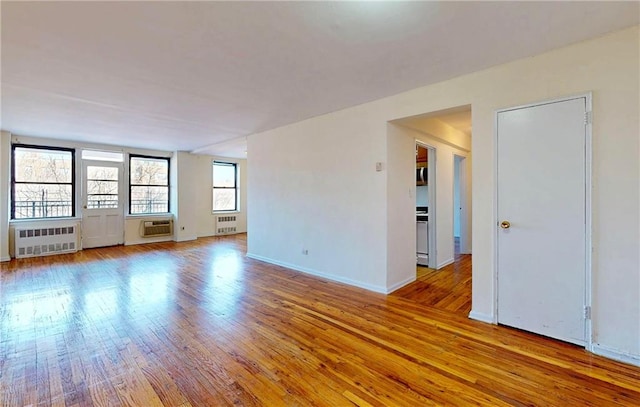 unfurnished room with an AC wall unit, baseboards, hardwood / wood-style floors, and radiator heating unit