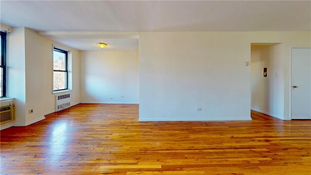 spare room featuring radiator, an AC wall unit, baseboards, and wood finished floors