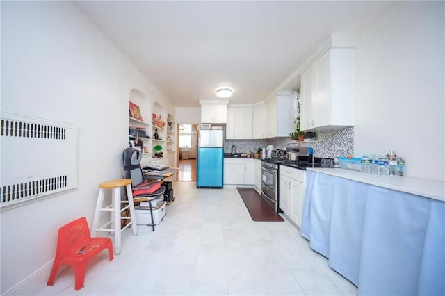 kitchen featuring freestanding refrigerator, a sink, white cabinets, stainless steel gas range oven, and backsplash