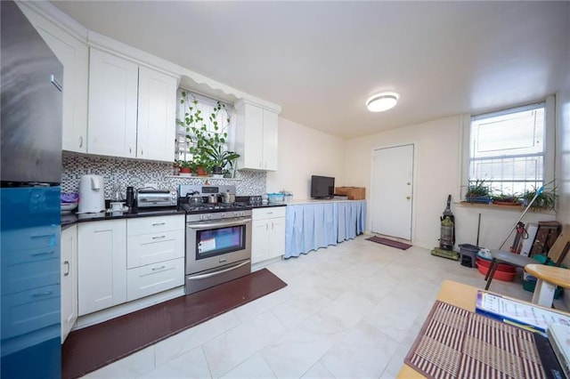 kitchen featuring backsplash, dark countertops, white cabinetry, a toaster, and gas range