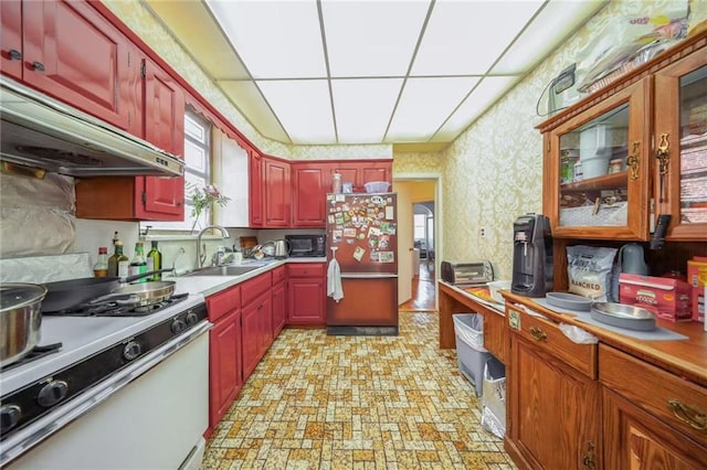 kitchen with under cabinet range hood, gas range gas stove, freestanding refrigerator, black microwave, and wallpapered walls