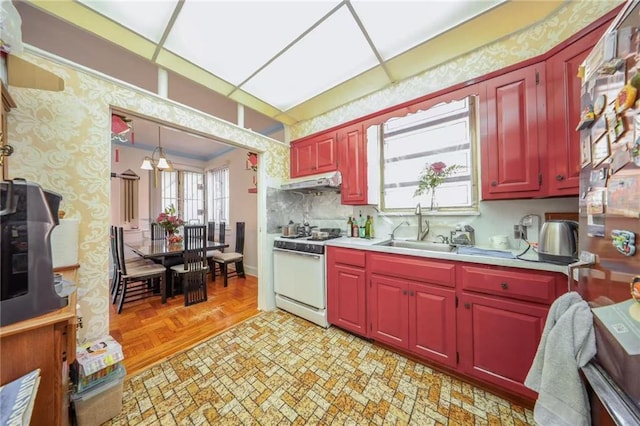 kitchen featuring under cabinet range hood, wallpapered walls, gas range gas stove, and a sink