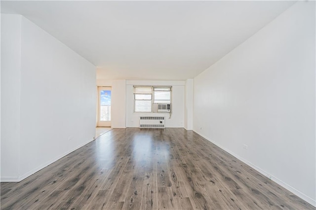 unfurnished living room with radiator heating unit, cooling unit, and wood finished floors