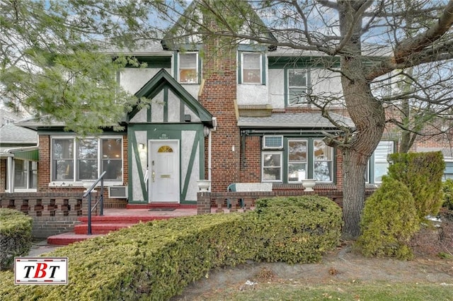 tudor-style house featuring brick siding, roof with shingles, and stucco siding