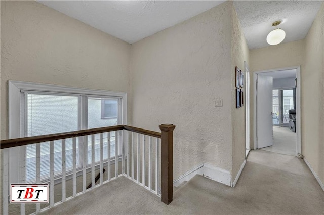 hall featuring baseboards, carpet flooring, a textured wall, and an upstairs landing