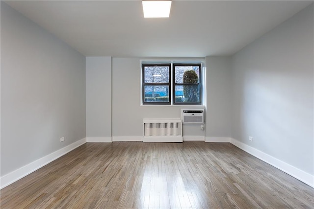 empty room featuring radiator heating unit, baseboards, wood finished floors, and a wall mounted AC